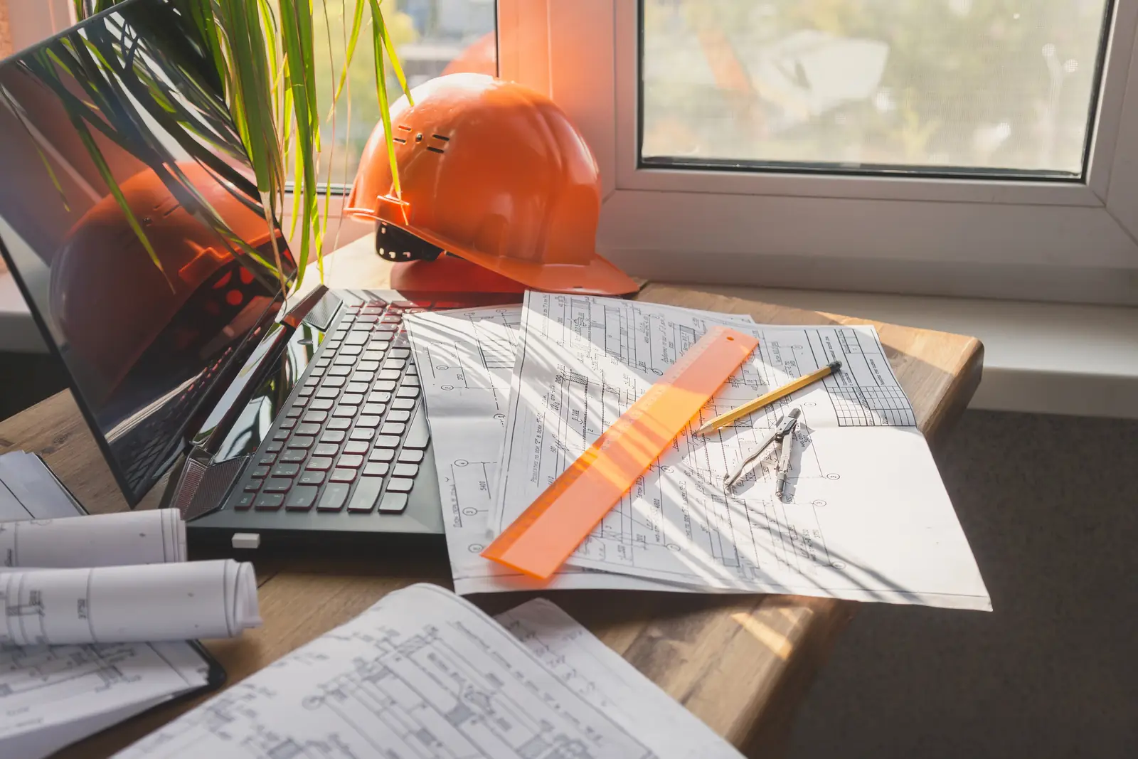 Construction blueprints, laptop and hard hat on a desk